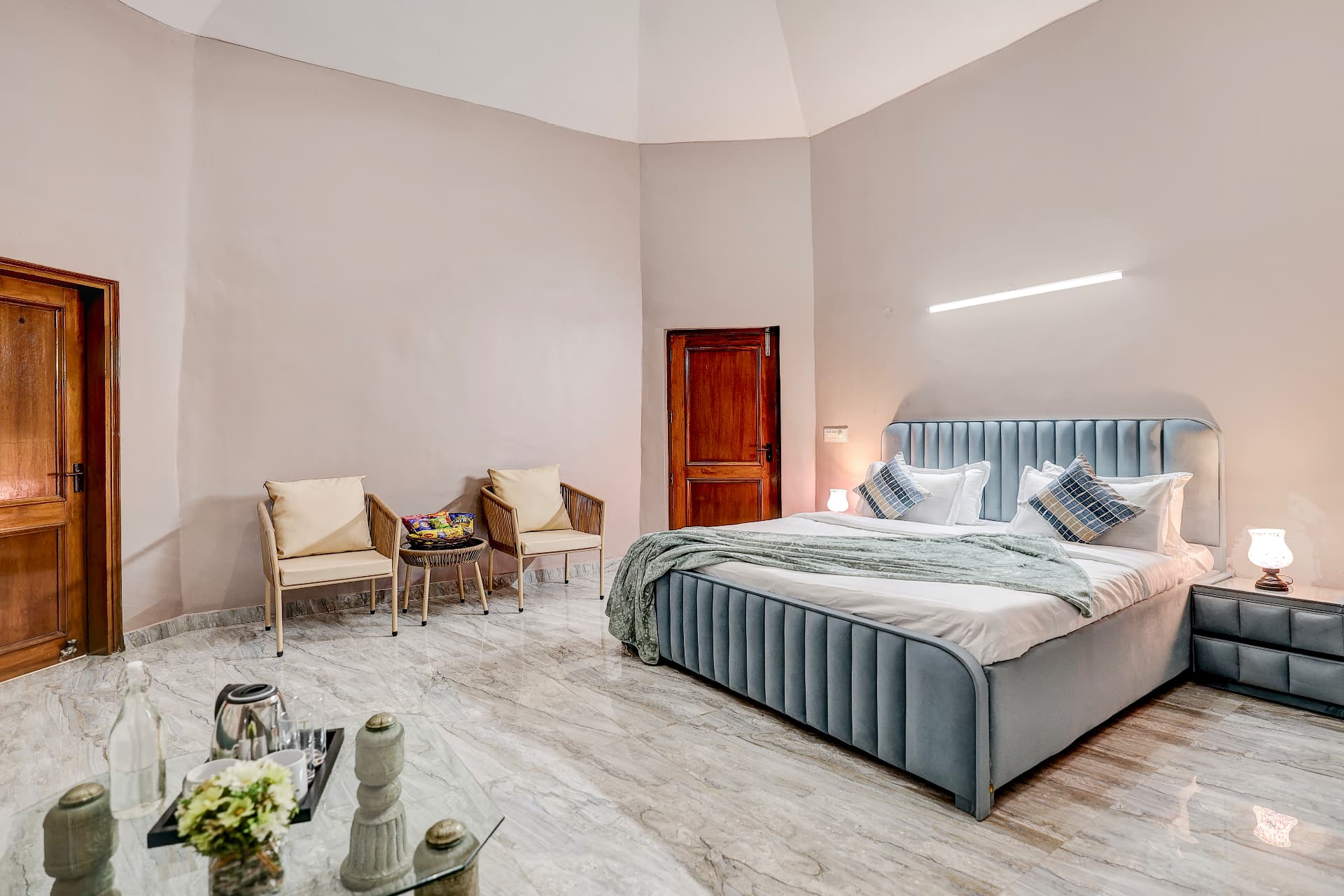 Blush bedroom with upholstered grey king bed and woven armchairs